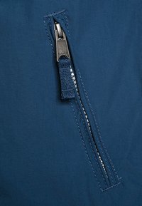 Tejido azul marino con una textura suave que presenta un zipper metálico. El tirador del zipper está unido a una cinta de tela, integrada en la costura.