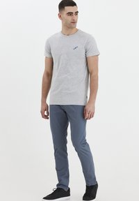 Tricou gri din bumbac cu mâneci scurte și guler rotund, având un mic logo albastru pe piept. Asortat cu pantaloni albastri slim-fit și adidași negri.