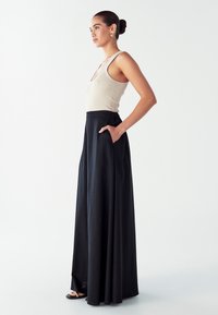 Brezbarvni bež top s rebrastim vzorcem v kombinaciji z visokim črnim maxi krilom, ki se lepo spušča in ima stranske žepe. Črne ravne sandale dopolnjujejo videz.