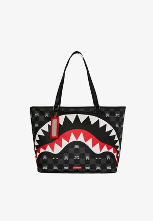 Bolsa tote negra con patrón de cuadros, diseño de boca de tiburón en rojo, blanco y negro, y una etiqueta rectangular roja colgando de una asa.