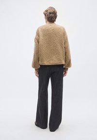 Jachetă maro din fleece texturat, cu croială lejeră, mâneci lungi și manșete reiate, asortată cu pantaloni largi, de culoare închisă.