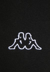 Czarna tkanina z białym haftowanym logo Kappa, przedstawiająca stylizowany wzór dwóch siedzących postaci o zminimalizowanych konturach.