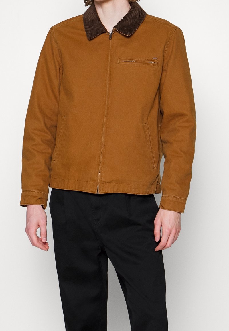 Brun zip-up jakke med et kordfløjlskrage, sidelommer og en brystlomme. Lavet af tekstureret stof med en lige pasform.