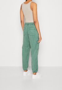 Groene cargobroek met een relaxte pasvorm, voorzien van een elastische tailleband, twee achterzakken en geribde manchetten. Gecombineerd met witte sneakers.