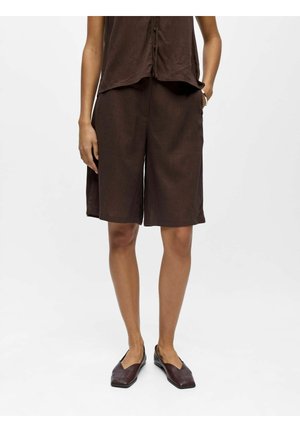 Personne portant un short ample marron foncé jusqu'aux genoux, un top sans manches assorti et des chaussures marron foncé à enfiler sur fond gris clair.