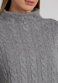 Maglione grigio lavorato a maglia con collo alto, caratterizzato da un motivo a treccia e delicate decorazioni di piccole borchie argento sparse.