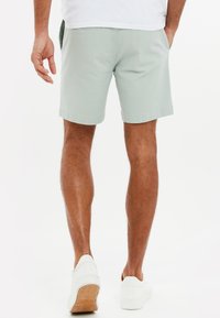 Lysegrønne shorts med et glat stof, rullet kant, sidelommer og en baglomme, kombineret med hvide sneakers på solbrune ben.