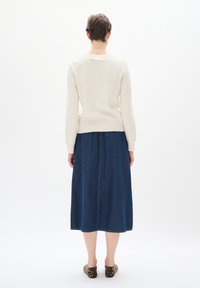 Krämfärgad stickad tröja i kombination med en lång denimkjol, med rak skärning och synlig sömdetalj. Bärs med mönstrade skor.