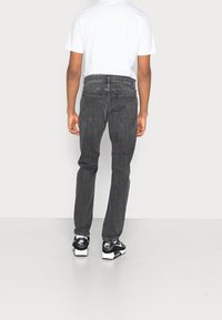 Vaqueros de mezclilla gris con un corte recto, que presentan bolsillos traseros y un acabado texturizado. Combinados con una camiseta blanca lisa y zapatillas negras.