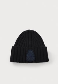 Beanie a coste nera con orlo ripiegato. Presenta un'etichetta ricamata blu scuro con un design di leone. Texture morbida.