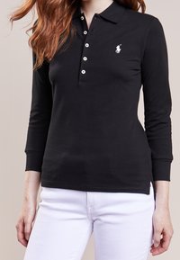 Svart långärmad polo skjorta i bomull, med en placket med tre knappar, vitt logotyp på vänster bröst och en något figurnära design.