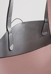 Roze leren handtas met een gladde textuur, voorzien van zwarte leren accenten en een open bovenkant met korte handvatten. Zichtbare stikdetails.