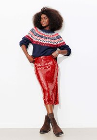 Pull en tricot bleu marine avec des motifs géométriques rouges et blancs, associé à une jupe crayon rouge pailletée brillante et des bottines marron.