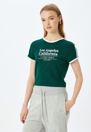 Vihreä puuvillapaita, jossa on valkoinen reunus, sisältää Los Angeles Kalifornia -tekstin ja College League -grafiikan. Lyhyet hihat ja lyhyt malli.
