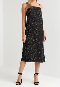 Svart klänning med spaghetti-band och flerfärgade prickar, knälång, i lättviktstyg, kombinerad med svarta klackar med ankelrem.