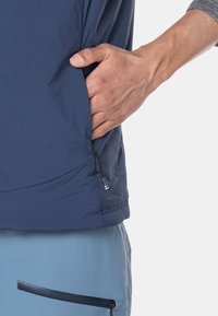 Marineblaue, leichte Jacke mit einer seitlichen Reißverschlusstasche, glatter Textur und tailliertem Design. Hand, die in die Tasche greift.