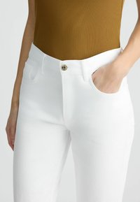 Vaqueros de mezclilla blanca con un ajuste estándar, diseño de cinco bolsillos y un cierre de botón clásico en la cintura. Textura suave y tejido resistente.