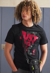 Svart t-skjorte med stor rød "JUST DO IT" tekst, med Liverpool FC-logo. Messenger bag i svart med neongrønne detaljer.