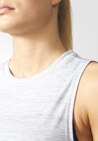 Valkoinen harmaa ilmanhiha toppi, jossa on sileä pinta, pyöreä pääntie ja hienovarainen heather-kuvio, asetettuna neutraalia taustaa vasten.