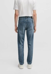 Lichtblauwe denim jeans met twee achterzakken, een rechte snit en een subtiele vervaagde textuur. Gepaard met een effen wit T-shirt en witte sneakers.