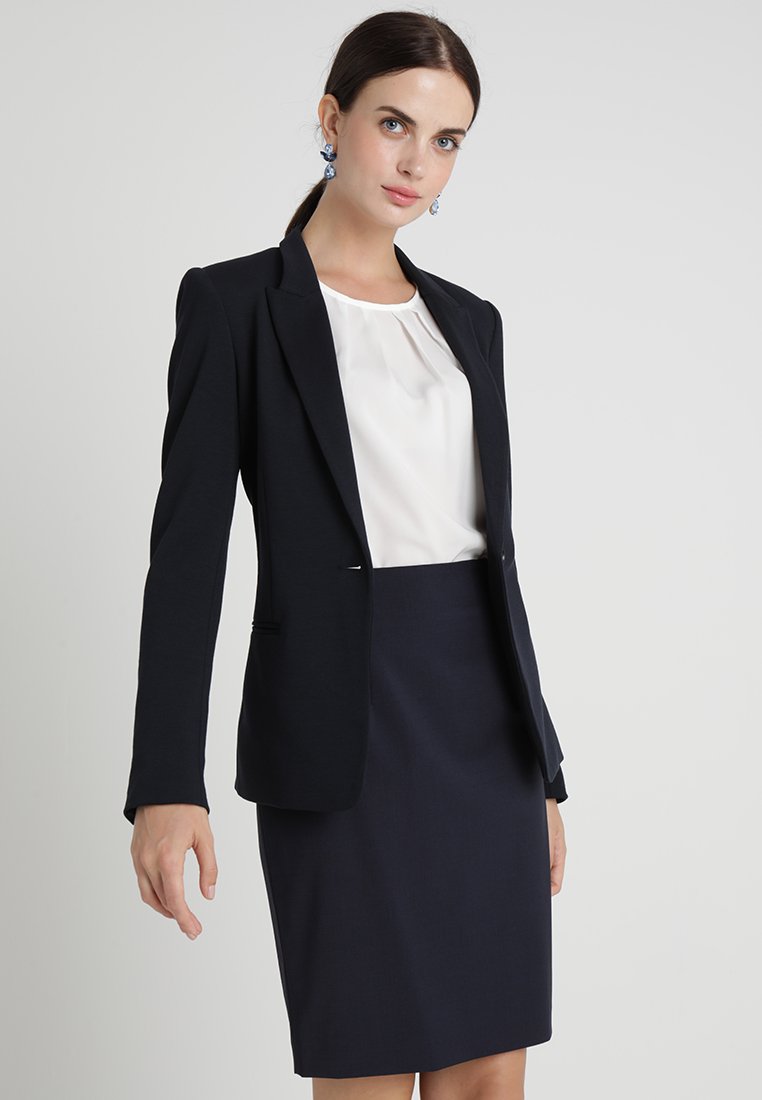 Námořnický blazer se strukturovanými rameny, slim fit a dvěma bočními kapsami, kombinovaný s bílou blůzou a tužkovou sukní. Hladká textura látky.
