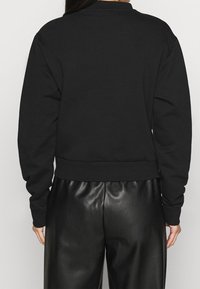 Sudadera negra con cuello redondo y puños acanalados, combinada con pantalones negros de polipiel. Textura suave, ajuste relajado y diseño cropped.