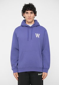 Fialová mikina vyrobená z mäkkého zmesového bavlneného materiálu, s prednou kapsou, kapucňou so šnúrkou a bielym logom na ľavej hrudi.