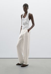 Bílý top na ramínka s vlnkovým výstřihem, doplněný volnými krémovými kalhotami s širokými nohavicemi. Černé sandály dotvářejí celý outfit.
