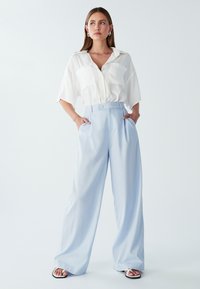 Svetlo modri široki hlače iz mehkega blaga, z visokim pasom, gumbnim zapiranjem in stranskimi žepi, v kombinaciji z belo s kratkimi rokavi.