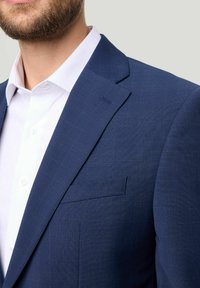 Close-up van de bovenkant van het lichaam van een man in een marineblauwe blazer over een wit overhemd, waarbij de textuur van de stof en de details van de revers zichtbaar zijn.