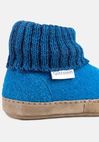 Pantofole blu in feltro con risvolto lavorato a maglia, dotate di una suola in suede marrone chiaro e un'etichetta bianca con la scritta "Gottstein". Texture complessiva liscia.