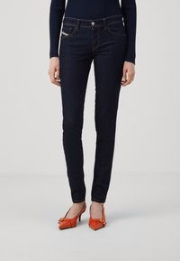 Mörka denimjeans med slim fit, fem fickor och orange sömmar. Matchas med orangea högklackade skor med en rosettaccent.