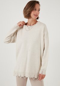 Maglione beige chiaro con una vestibilità ampia, caratterizzato da un colletto a costine, orlo sfilacciato e maniche lunghe, realizzato in morbido materiale a maglia.