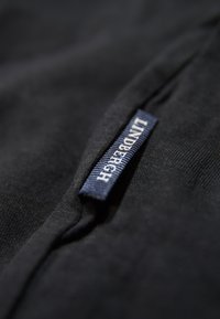 Zwarte stoffen label met "LINDENBERGH" in witte tekst, met een textuur achtergrond en een gladde rand. Close-up weergave benadrukt de stiksels.