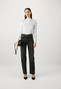 Hvit langermet topp med høy hals, svarte høytaljede jeans, og svarte spisse hæler. Liten svart veske med snøring.