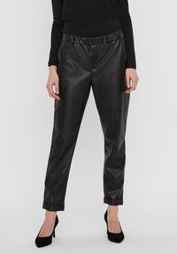 Black faux leather trousers with a relaxed fit, elastic waistband, rolled cuffs, and a smooth, shiny texture. Paired with black heels.
