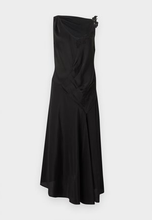 Moteris su tamsiais plaukais, vilkinti juodą asimetrišką midi suknelę su nėrinių detalėmis ant vieno peties ir juodais aukštakulniais sandalais su dirželiais.