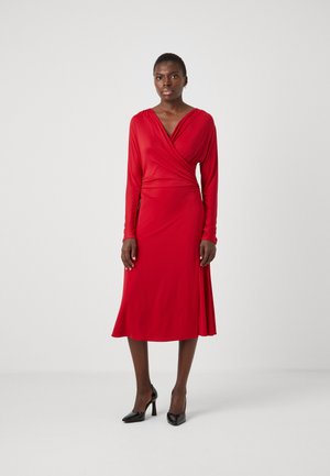 Red dress made of smooth fabric, featuring a wrap design, long sleeves, and a mid-length skirt. Model wears black high-heeled shoes.