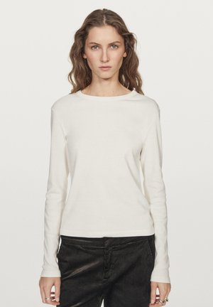 Cremfarbener Langarmshirt aus weichem Stoff mit rundem Ausschnitt. Kombiniert mit dunkelbraunen Cordhosen, die eine glatte Oberfläche und eine lockere Passform haben.