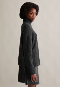 Dunkelgrauer Rollkragenpullover mit weicher Textur, gerippten Bündchen und lockerer Passform, kombiniert mit einem schwarzen Lederrock.