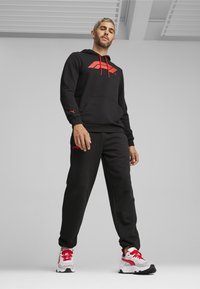 Sort hoodie med røde detaljer og logo, matchende sorte bukser og hvide sneakers med røde elementer. Materialet ser blødt og struktureret ud.