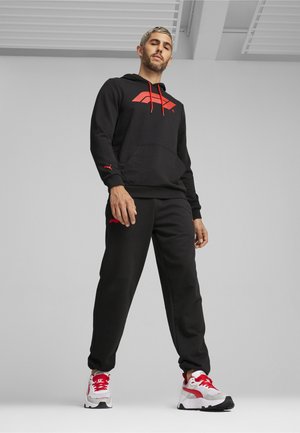 Sort hoodie med røde detaljer og logo, matchende sorte bukser og hvide sneakers med røde elementer. Materialet ser blødt og struktureret ud.