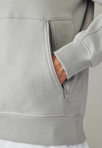 Grå sweatshirt med ribbet kant, lynlåslomme og tekstureret stof. Lange ærmer med ribbede manchetter, glat overflade og afslappet pasform.
