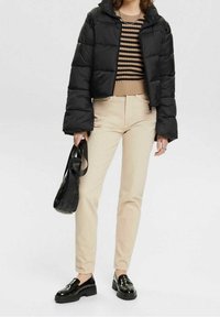 Zwarte pufferjas, beige gestreepte trui, lichtbeige broek en zwarte loafers. Zwarte tas met een gestructureerde afwerking.