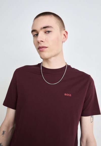 T-shirt col rond bordeaux en coton, avec un petit logo "BOSS" rouge sur la poitrine et un collier en chaîne argentée.