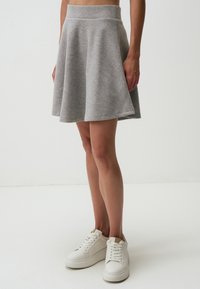 Grijze klokrok van zacht materiaal met een brede tailleband, gecombineerd met witte sneakers, gepresenteerd tegen een lichte achtergrond.