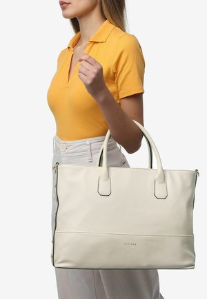 Weiße Leder-Tote-Bag mit strukturiertem Finish, grünen Akzenten und doppelten Griffen, gehalten von einer Person in einem gelben Poloshirt und weißen Hosen.
