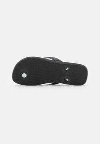 Svart flip-flop såle med et teksturert mønster, som har to sirkulære hull og to festepunkter ved sålens bunn.