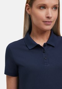 Granatowa koszulka polo z krótkim rękawem, kołnierzykiem i trzema czarnymi guzikami. Wykonana z teksturowanej tkaniny dla swobodnego dopasowania.