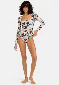 Garām piedurknēm darināts peldkostīms ar melnu fonu un lieliem ziedu rakstiem lavandas un zaļā krāsā, izgatavots no gludas, elastīgas auduma.